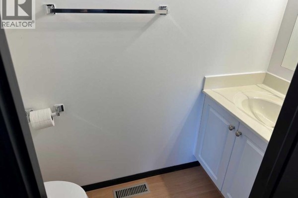 A small powder room with a white toilet, vanity, and sink, and a chrome towel bar. - 120, 10150 121 Avenue, Grande Prairie