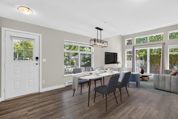 Open concept living and dining area with large windows, grey furniture, and wood flooring. - 120 20033 70 Avenue, Langley