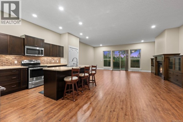 Modern kitchen with dark cabinetry, stainless steel appliances, and granite countertops. - 120 2205 Robert Lang Dr, Courtenay