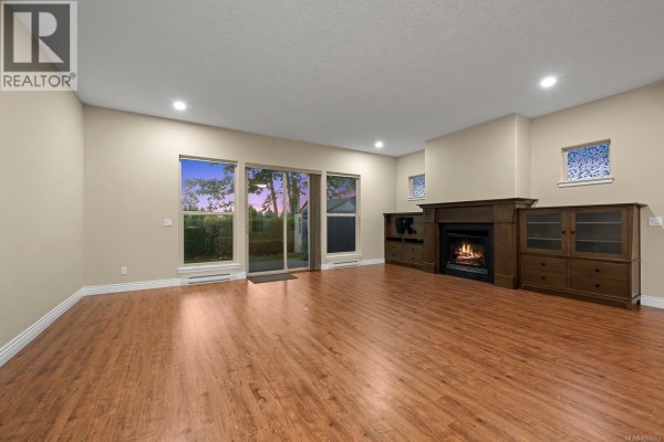 Cozy living room with a fireplace, large windows, and a view of the backyard. - 120 2205 Robert Lang Dr, Courtenay