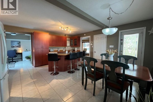 Dining area with a wooden table, black chairs, and open-concept kitchen. - 120 34th Avenue, Edmundston