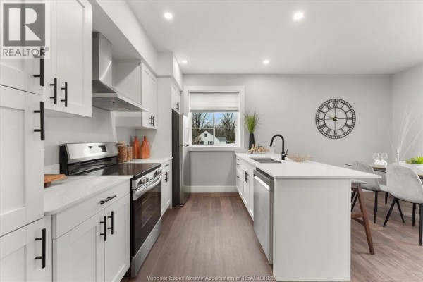 White kitchen with stainless steel appliances, quartz countertops, and an island with a sink. - 120 Centre Street Unit# 1b, Essex