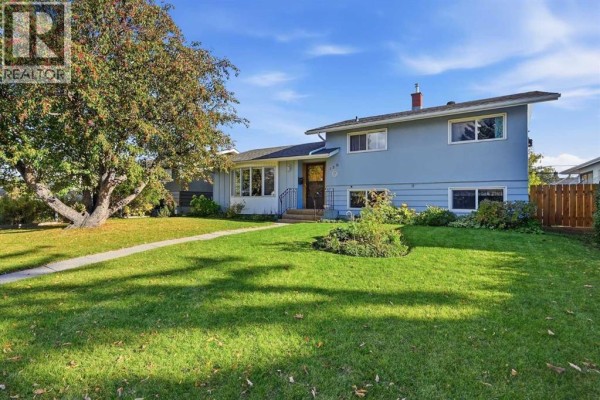 Side view of the light blue two-story house with a green lawn and mature trees. - 120 Fairview Crescent Se, Calgary