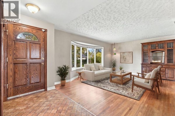 Living room entrance with a wooden front door and a bay window overlooking the front yard. - 120 Fairview Crescent Se, Calgary