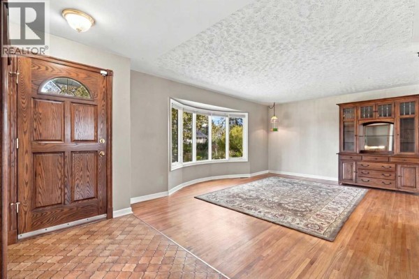 Living room featuring a bay window, hardwood floors, a large rug, and a wooden china cabinet. - 120 Fairview Crescent Se, Calgary