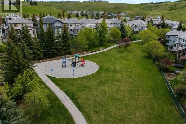 Park with a playground, benches, and walking paths next to houses. - 120 Gleneagles Terrace, Cochrane