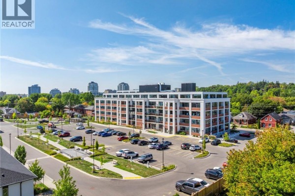 Aerial view of a modern white brick apartment building surrounded by trees and parking. - 120 Huron Street Unit# 507, Guelph