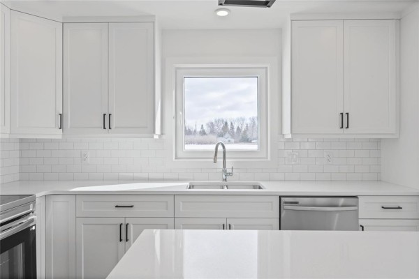 Kitchen sink and countertop area with a window view of a snowy landscape and trees. - 120 Langill Way, Steinbach