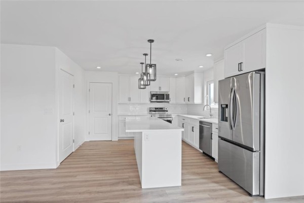 Wide view of a bright white kitchen featuring an island, stainless steel appliances, and light wood flooring. - 120 Langill Way, Steinbach