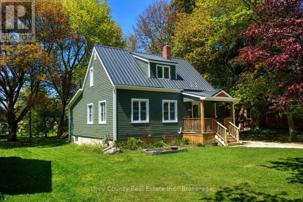 View of the green house through trees, with a detached garage to the right. - 120 Mark Street W, Grey Highlands