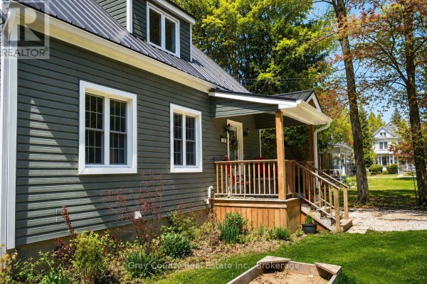 The green house from the front right, showing the porch, windows, and garage. - 120 Mark Street W, Grey Highlands