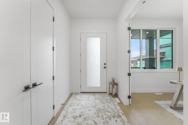 Bright white entryway with a frosted glass door, wood floors, and a patterned rug. - 120 Ravenshire Wynd, Sherwood Park