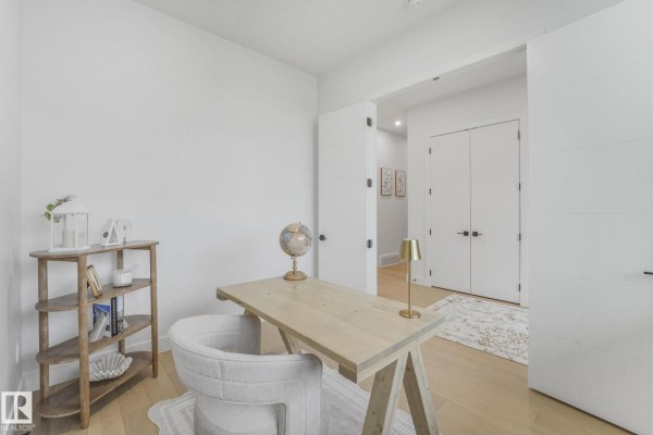 Home office with a light wood desk, beige armchair, and white walls. - 120 Ravenshire Wynd, Sherwood Park
