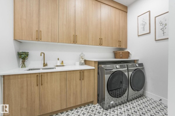 Laundry room with light wood cabinetry, stainless steel washer and dryer, and patterned floor tiles. - 120 Ravenshire Wynd, Sherwood Park