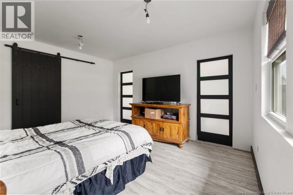 Bedroom with a bed, wooden media stand, black barn door, and frosted glass doors. - 120 Saint-marcel, Acadieville