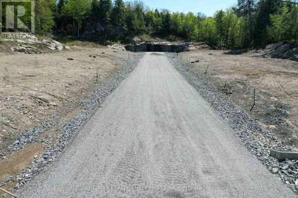 Gravel driveway entrance with stone borders, leading into a cleared construction site surrounded by trees. - 120 Townline Road E, Huntsville