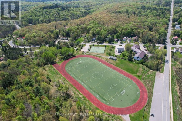 Aerial view of a suburban area with a running track and sports field, surrounded by green trees and homes. - 120 Townline Road E, Huntsville