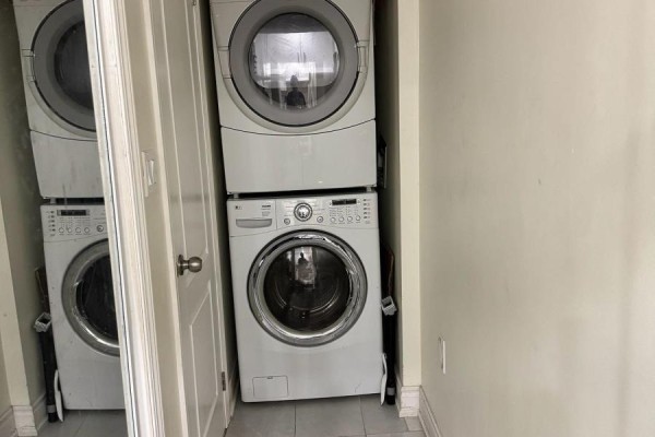 Laundry room with stacked white front-load washer and dryer units. - 120 Viceroy Crescent, Brampton