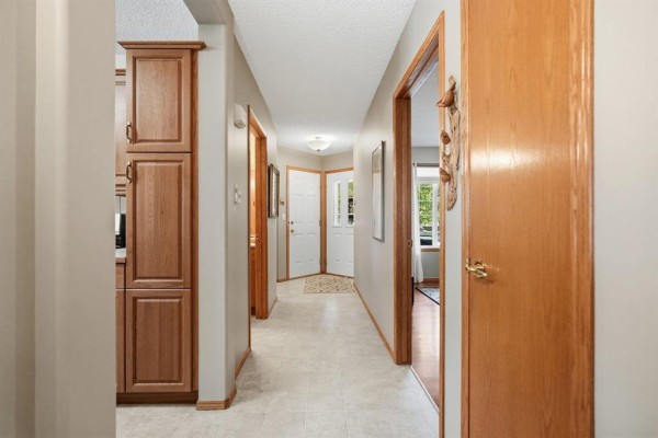 Hallway with light beige tile flooring, wood trim, and doors leading to various rooms. - 120 Wyndstone Circle, East St Paul