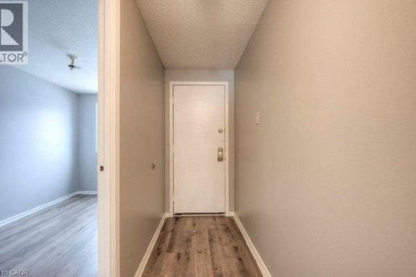 Interior hallway with a white front door, beige walls, and wood-look flooring. - 1200 Courtland Avenue Unit# 3, Kitchener