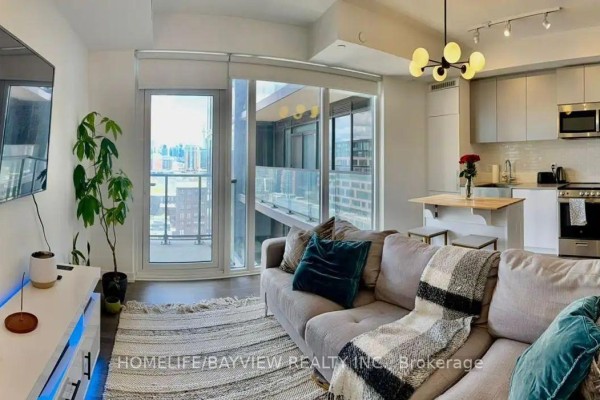 Living room with a grey sectional sofa, rug, and a view of the city through glass doors. - 1201 - 270 Dufferin Street, Toronto