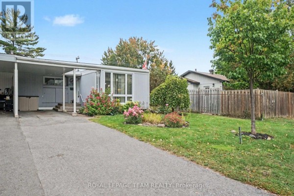 View of the house from the driveway showing the carport, garden, and neighbouring fence. - 1201 Meadowlands Drive E, Ottawa