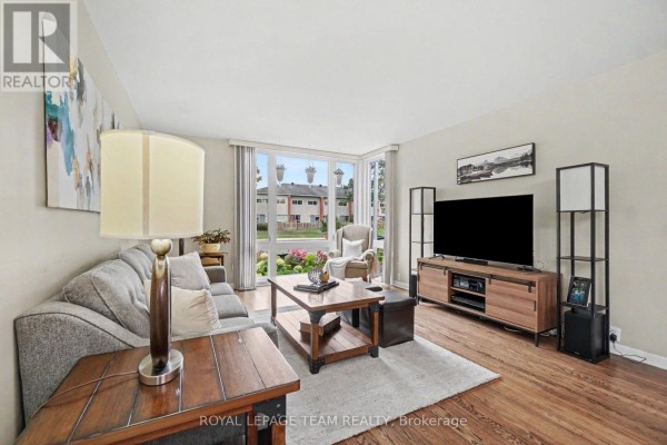 Living room with a grey sofa, wooden coffee table, and a large television across from a bay window. - 1201 Meadowlands Drive E, Ottawa