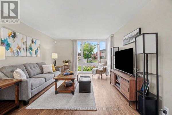 Living room featuring a grey sofa, dark wood furniture, and hardwood floors with a view to the exterior. - 1201 Meadowlands Drive E, Ottawa