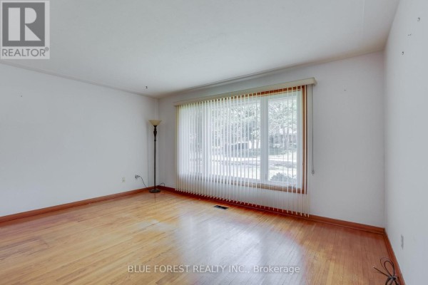 Empty living room with hardwood floors, white walls, and vertical blinds on window. - 1201 Patann Drive N, London East