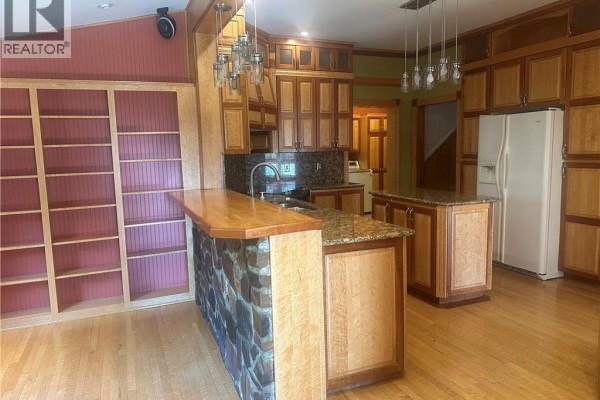 Kitchen with wooden cabinetry, granite countertops, and an island with bar seating. - 1201 West Riverside Drive, Perth Andover