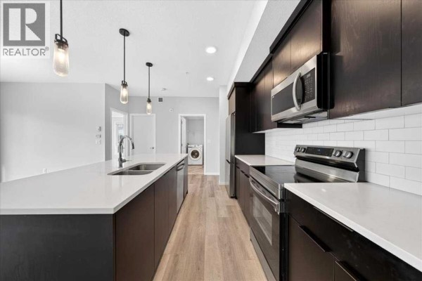 Kitchen with dark wood cabinets, white subway tile backsplash, and stainless steel appliances. - 1202, 220 Seton Grove Se, Calgary