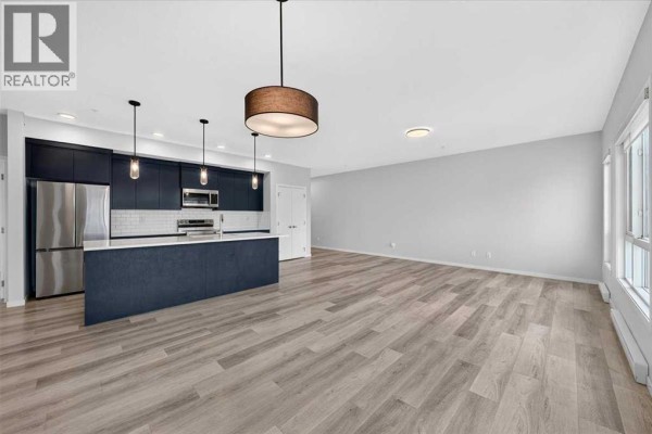 Open concept living area and kitchen with light wood flooring and large windows. - 1202, 220 Seton Grove Se, Calgary