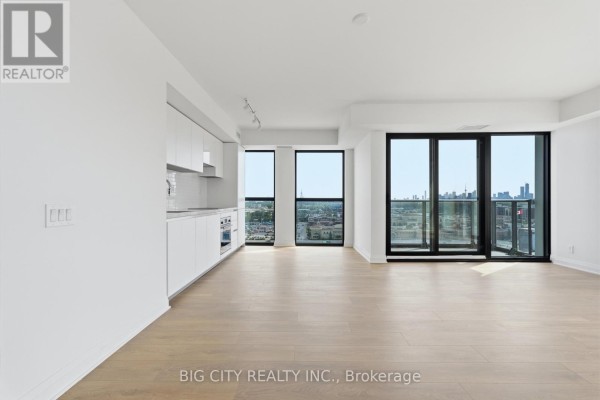 Open concept living area with modern white kitchen cabinets and large windows. - 1202 - 25 Frederick Way, Toronto