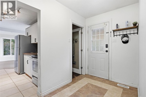 Entrance hall with white door, tiled floor, and doorway to kitchen and closet. - 1202 Crestwood Drive, Kamloops