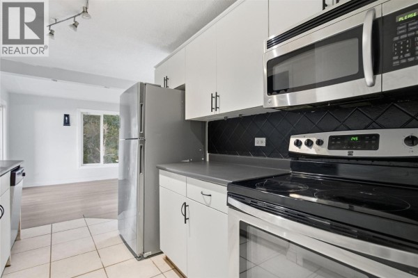 Kitchen with stainless steel refrigerator, microwave, and black tile backsplash. - 1202 Crestwood Drive, Kamloops