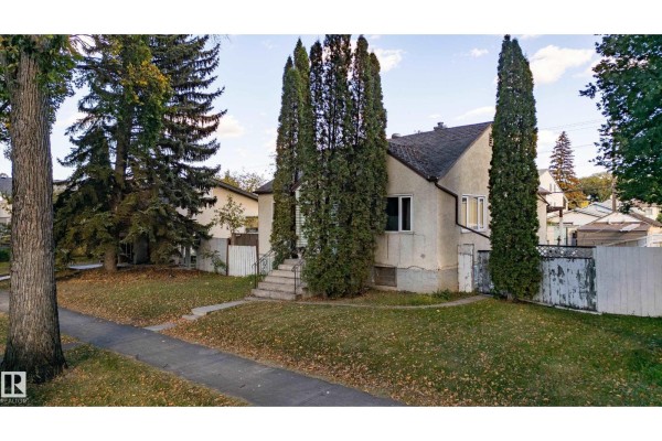 Side exterior view of a light blue house showing the driveway and a white wooden fence. - 12023 67 St Nw, Edmonton