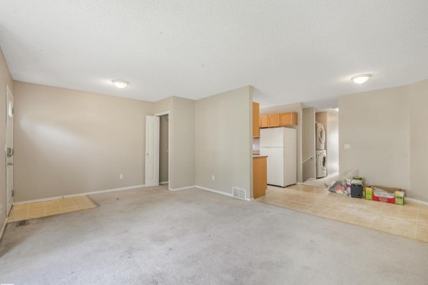 Open concept living area with beige carpet, kitchen, and laundry area. - 12027 105 St Nw, Edmonton