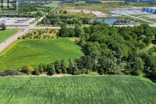 Aerial view of farmland featuring green fields, dense trees, a highway, and a commercial complex. - 12027 Sunset Road, St  Thomas