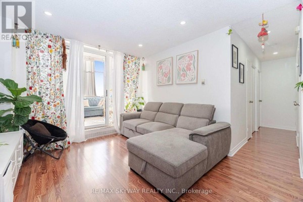Living room with grey sectional sofa, patterned curtains, and balcony access. - 1203 - 1615 Bloor Street, Mississauga