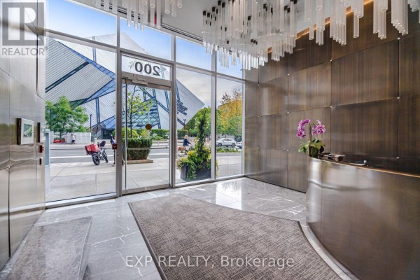 Building lobby with large glass windows, marble floors, and a silver reception desk. - 1203 - 200 Bloor Street W, Toronto