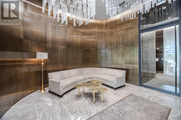 A seating area in the lobby with a curved sofa, small tables, and a floor lamp. - 1203 - 200 Bloor Street W, Toronto