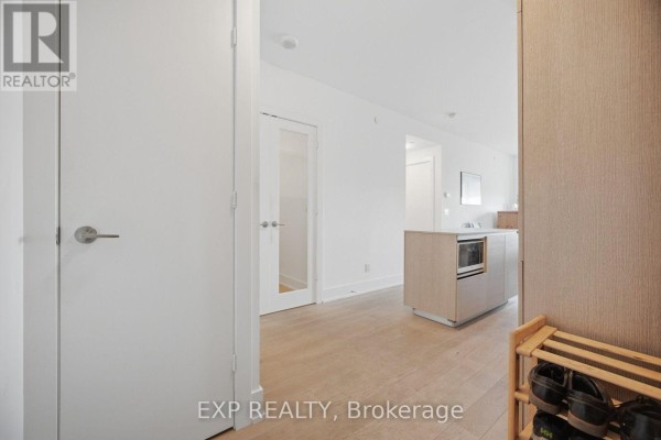 Interior hallway with white walls, light wood floors, and a kitchen island. - 1203 - 200 Bloor Street W, Toronto