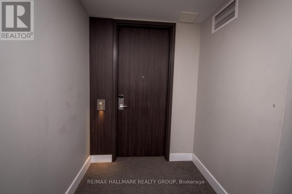 Apartment door in a hallway with dark wood, brushed metal hardware, and lighting. - 1203 - 300 Lisgar Street, Ottawa