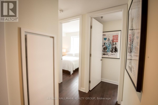 Hallway with dark wood floors, white doors, and views into a bedroom and another room. - 1203 - 300 Lisgar Street, Ottawa