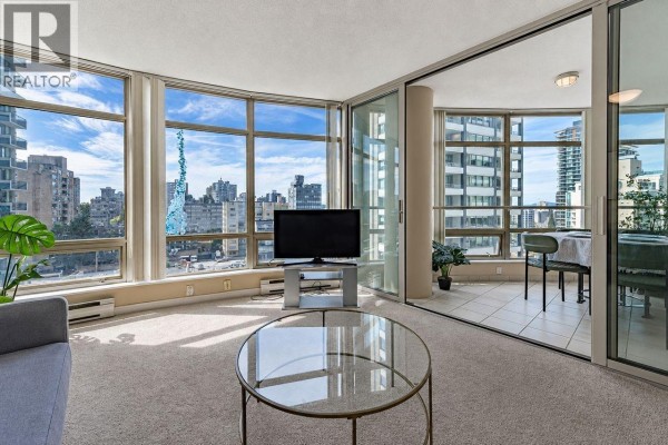 A living room with a sectional sofa, a coffee table, a television, and large windows with city views. - 1203 1288 Alberni Street, Vancouver