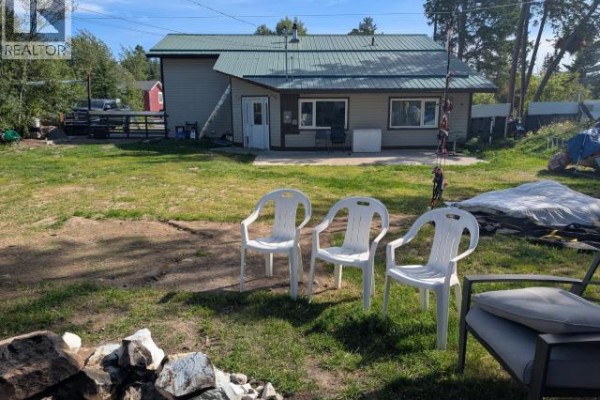 Backyard with white plastic chairs, a fire pit area, and a covered patio. - 1203 Spruce Street, Whitehorse