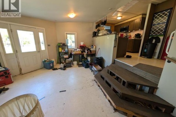 Interior view of a room with double doors, white floors, and wooden stairs leading to a kitchen area. - 1203 Spruce Street, Whitehorse