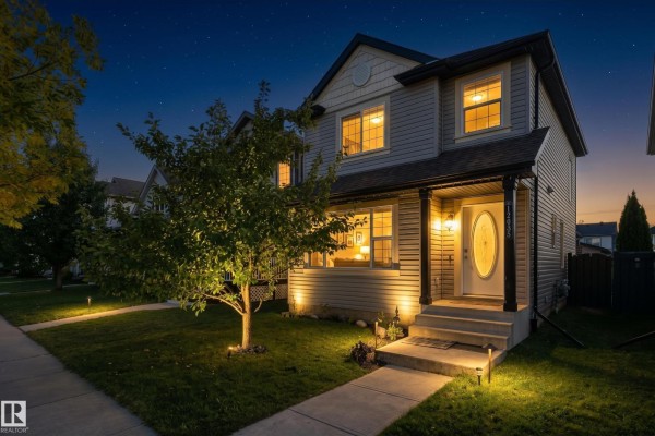 Front exterior of a two-story gray house at night with porch light on and landscape lighting. - 12035 18 Av Sw, Edmonton