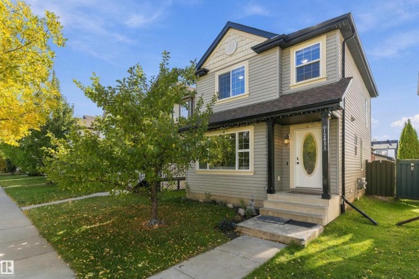 Front exterior of a two-story gray house with a white door and manicured lawn in daylight. - 12035 18 Av Sw, Edmonton