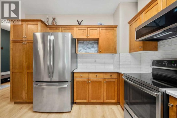 Corner view of a kitchen featuring a stainless steel stove, white quartz countertops, and wood cabinets. - 1204, 720 Willowbrook Road Nw, Airdrie